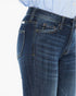 Close-up of a person wearing dark blue denim jeans with a light blue and white striped shirt visible at the waist, against a plain white background.