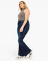 A woman modeling dark blue flare jeans with a ribbed mock neck top and white sneakers, shown from a side profile against a plain white background.