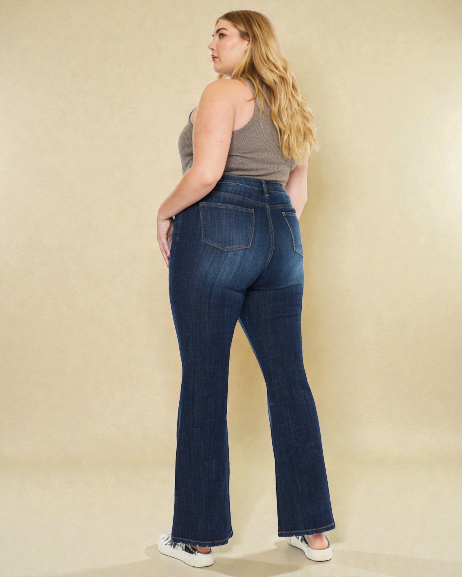 Woman wearing blue jeans and a gray tank top against a beige background