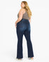 A woman modeling a pair of dark blue high-waisted flare jeans from the back, paired with a gray tank top and white sneakers, against a plain white background.
