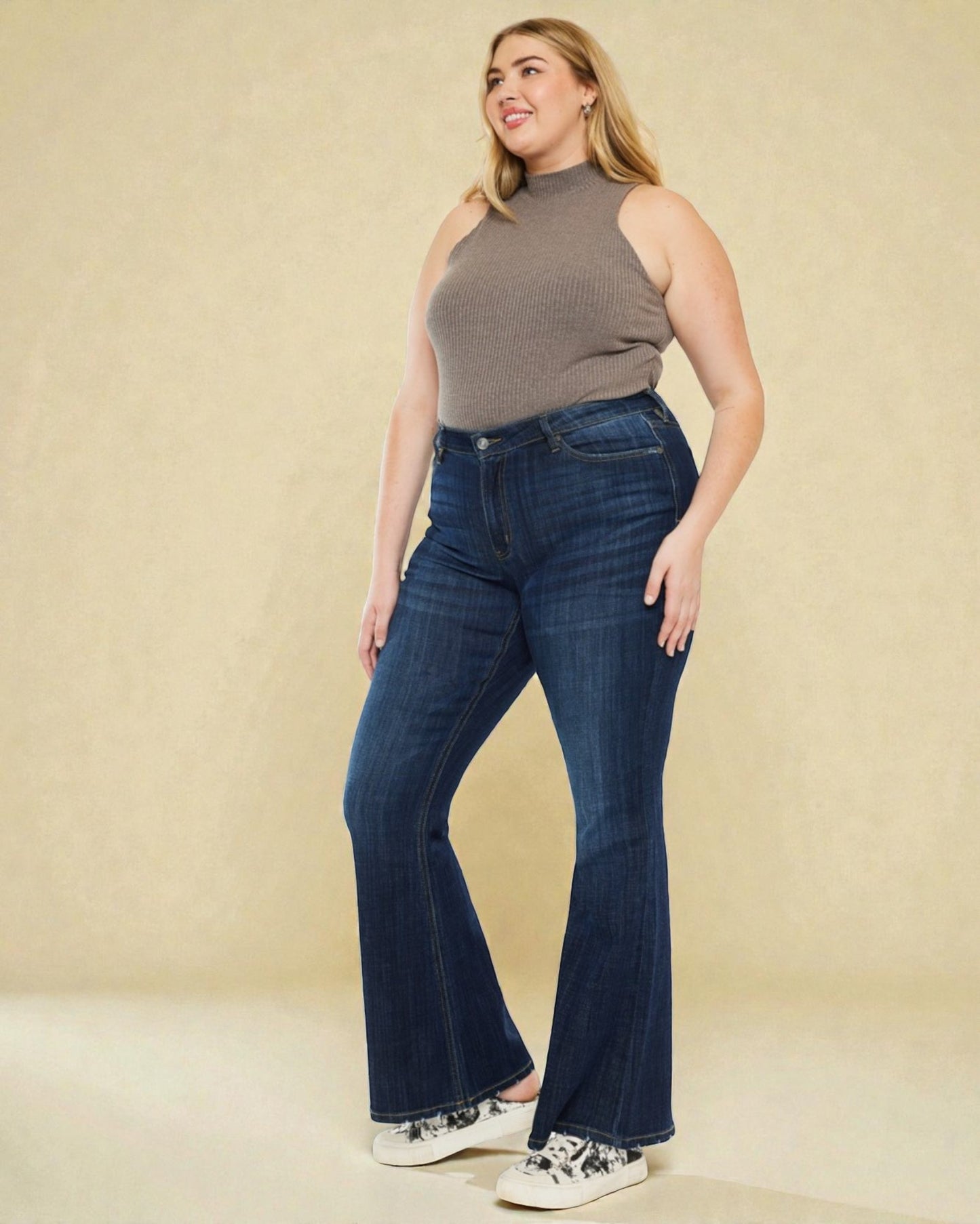 Woman wearing blue flared jeans and a brown sleeveless top on a beige background