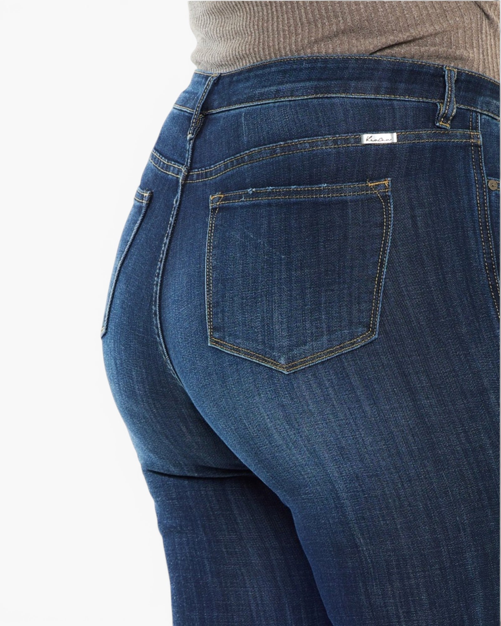 Close-up back view of a person wearing dark blue denim jeans with a ribbed beige top visible at the waist, against a plain white background.