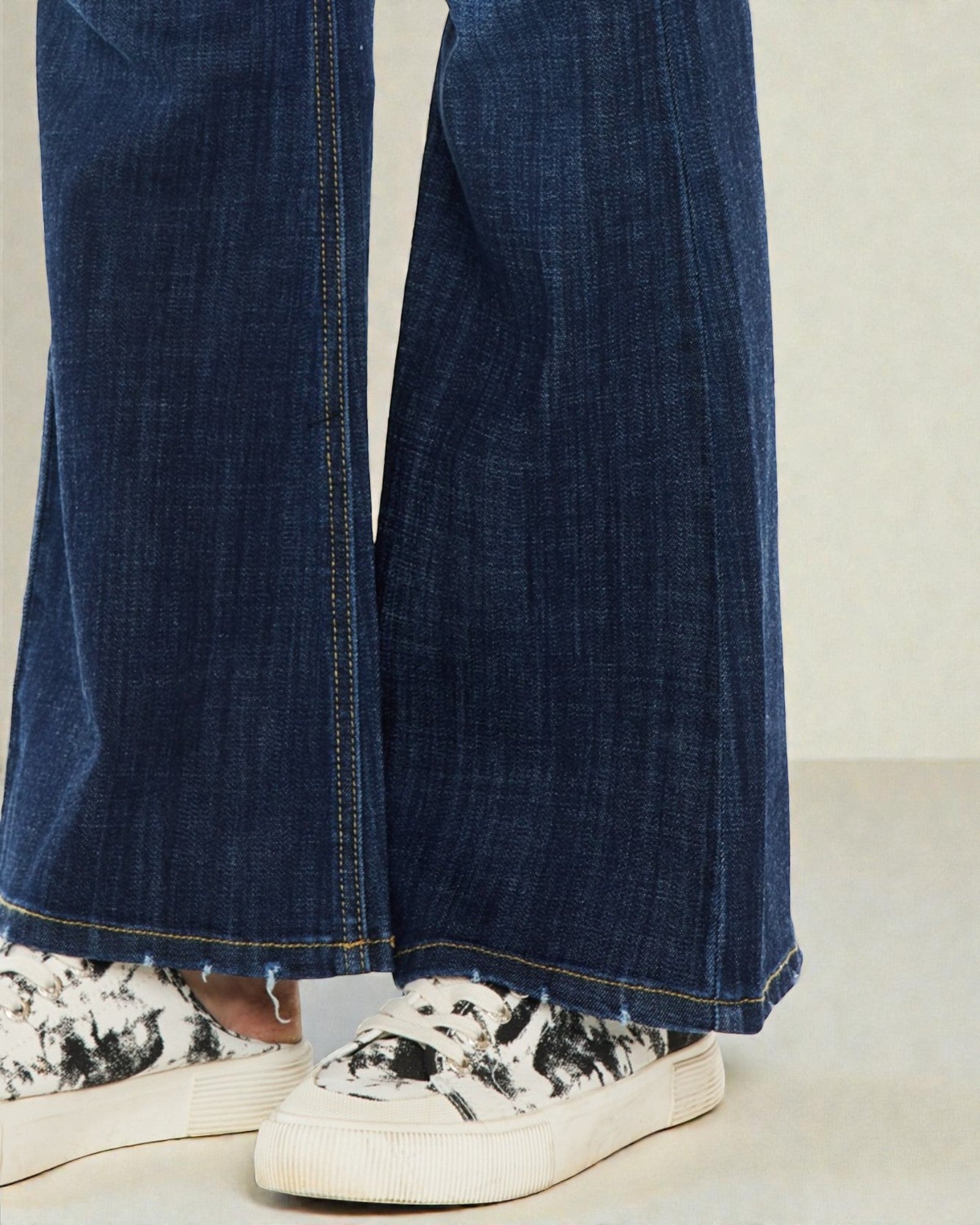 Blue jeans worn with white sneakers on a neutral background