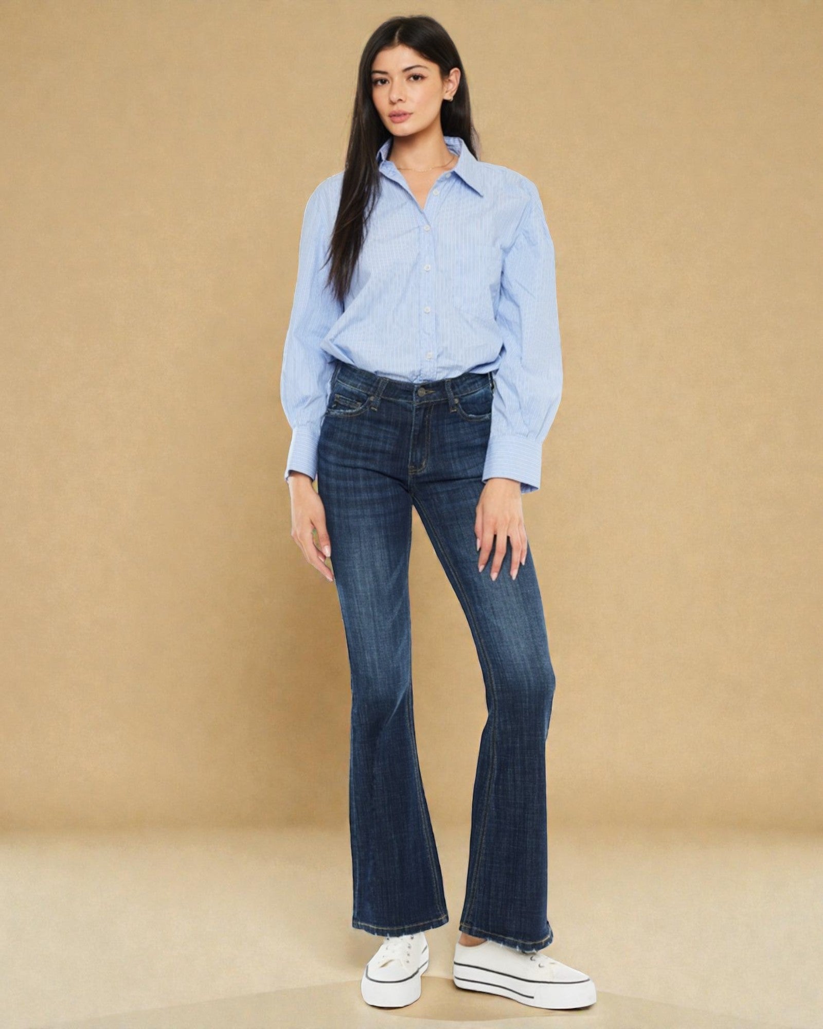 Woman wearing a light blue shirt and dark blue jeans against a beige background