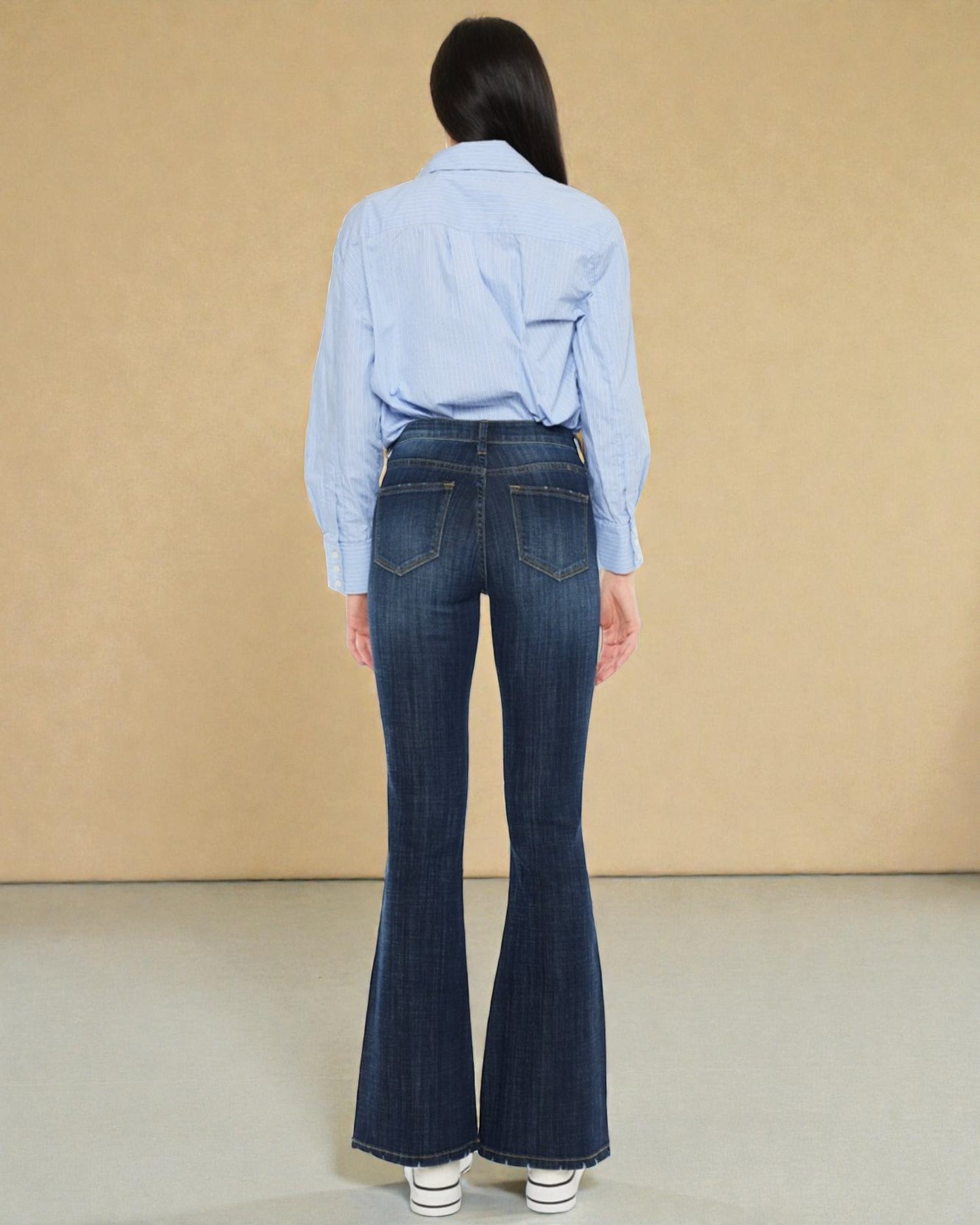 Person wearing a light blue shirt and dark blue flared jeans against a beige background