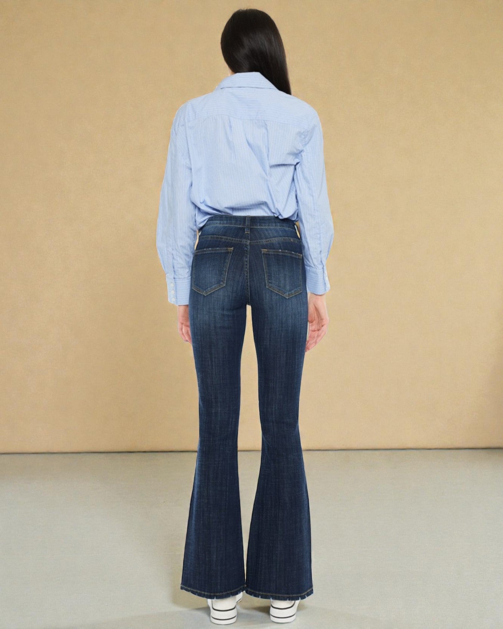 Person wearing a light blue shirt and dark blue flared jeans against a beige background