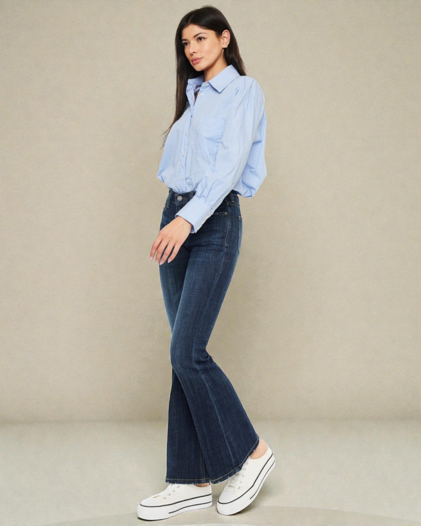 Woman wearing a light blue shirt and dark blue jeans against a beige background