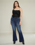 Woman wearing blue jeans and a black top on a plain background