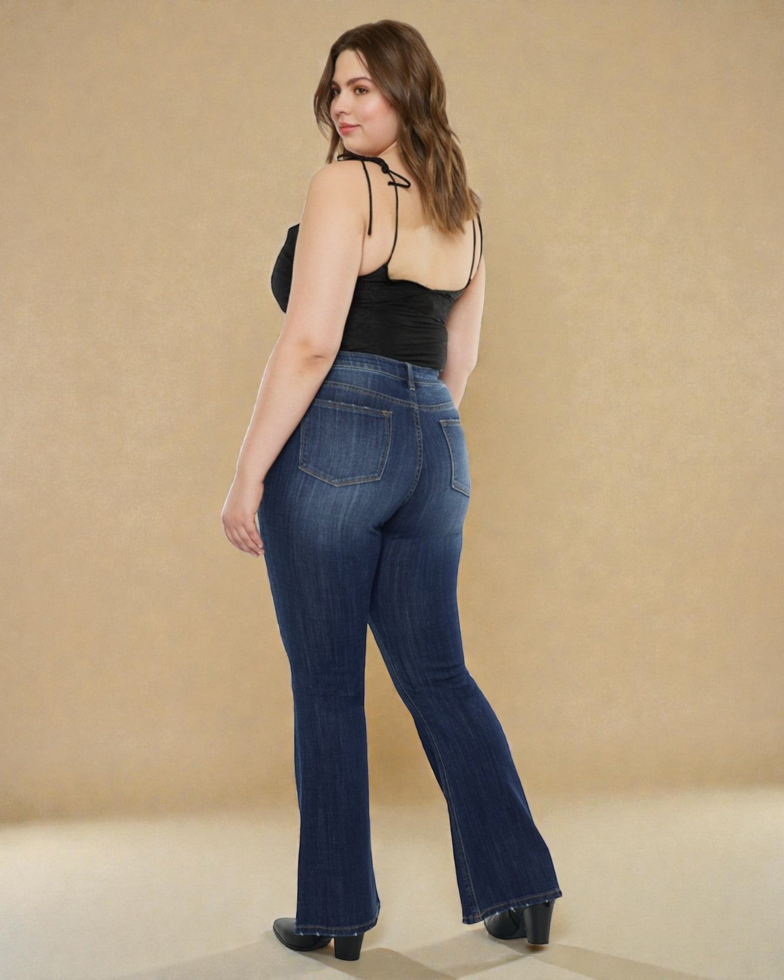 Woman wearing blue jeans and a black top against a beige background