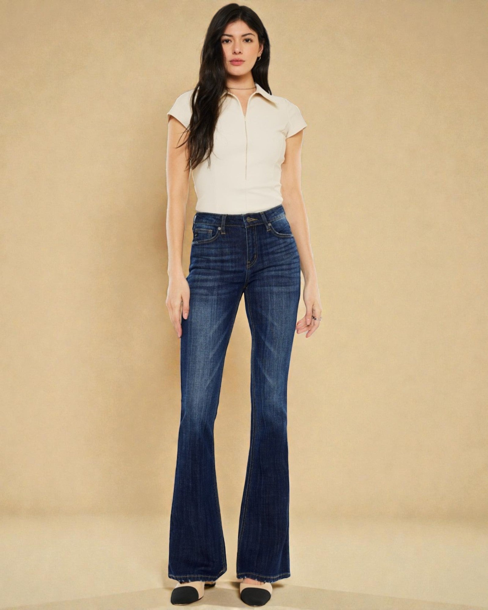 Woman wearing a white top and blue jeans against a beige background