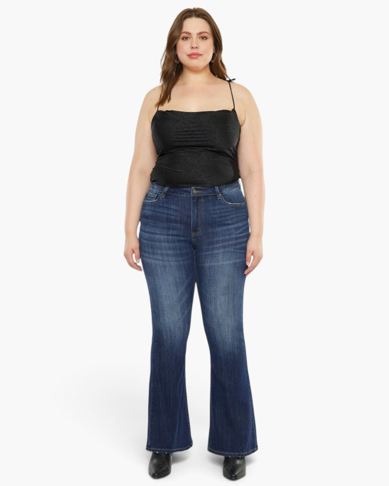 A woman modeling a black ribbed camisole top and dark blue flare jeans against a plain light gray studio background.