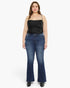A woman modeling a black ribbed camisole top and dark blue flare jeans against a plain light gray studio background.
