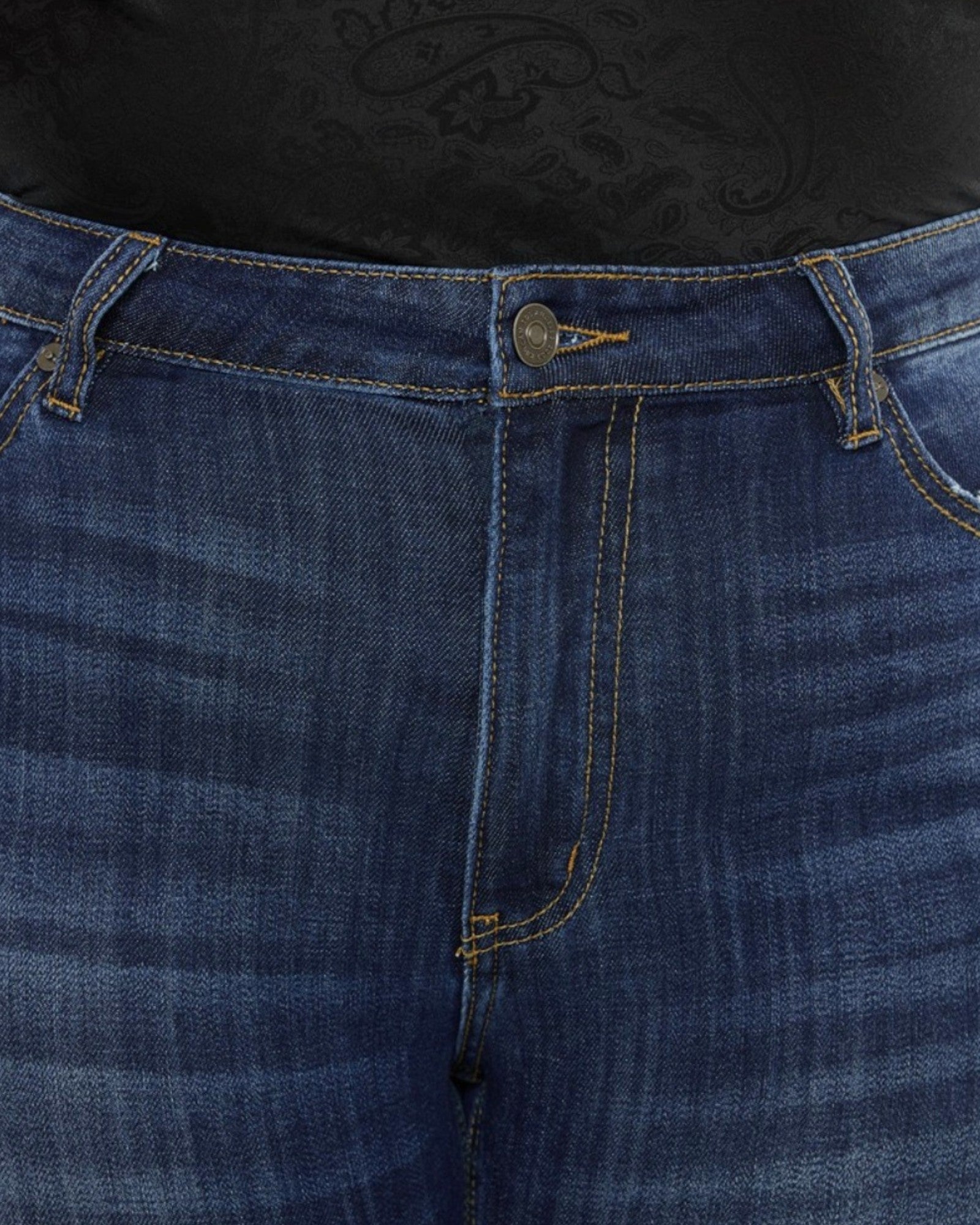 Close-up of dark blue denim jeans showing the front waistband, button closure, belt loops, and contrast stitching.