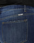 Close-up of the back pocket of dark blue denim jeans with yellow contrast stitching and a small metal brand tag reading 'Kancan'.