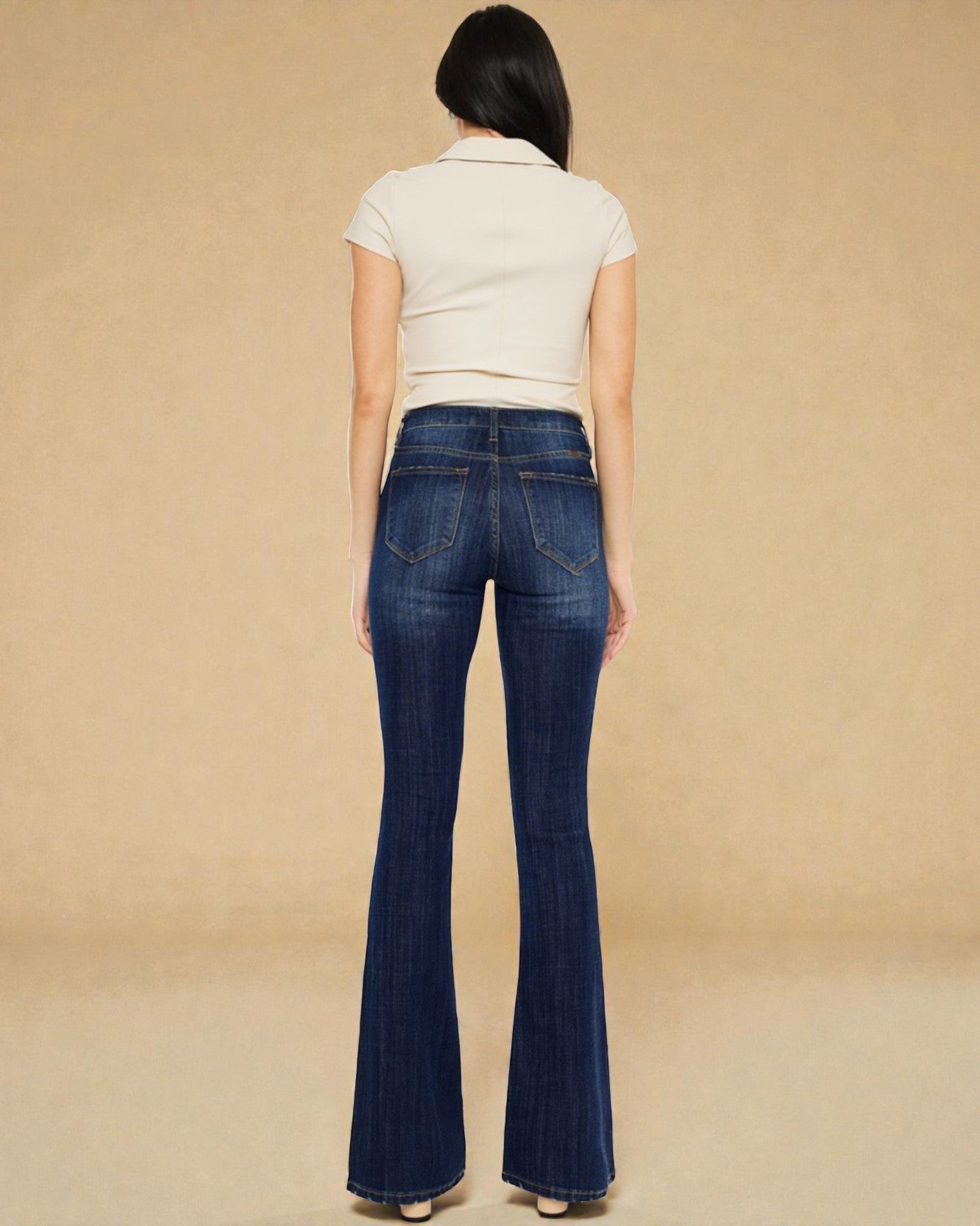 Woman wearing blue flared jeans and a white top on a beige background