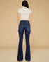 Woman wearing blue flared jeans and a white top on a beige background