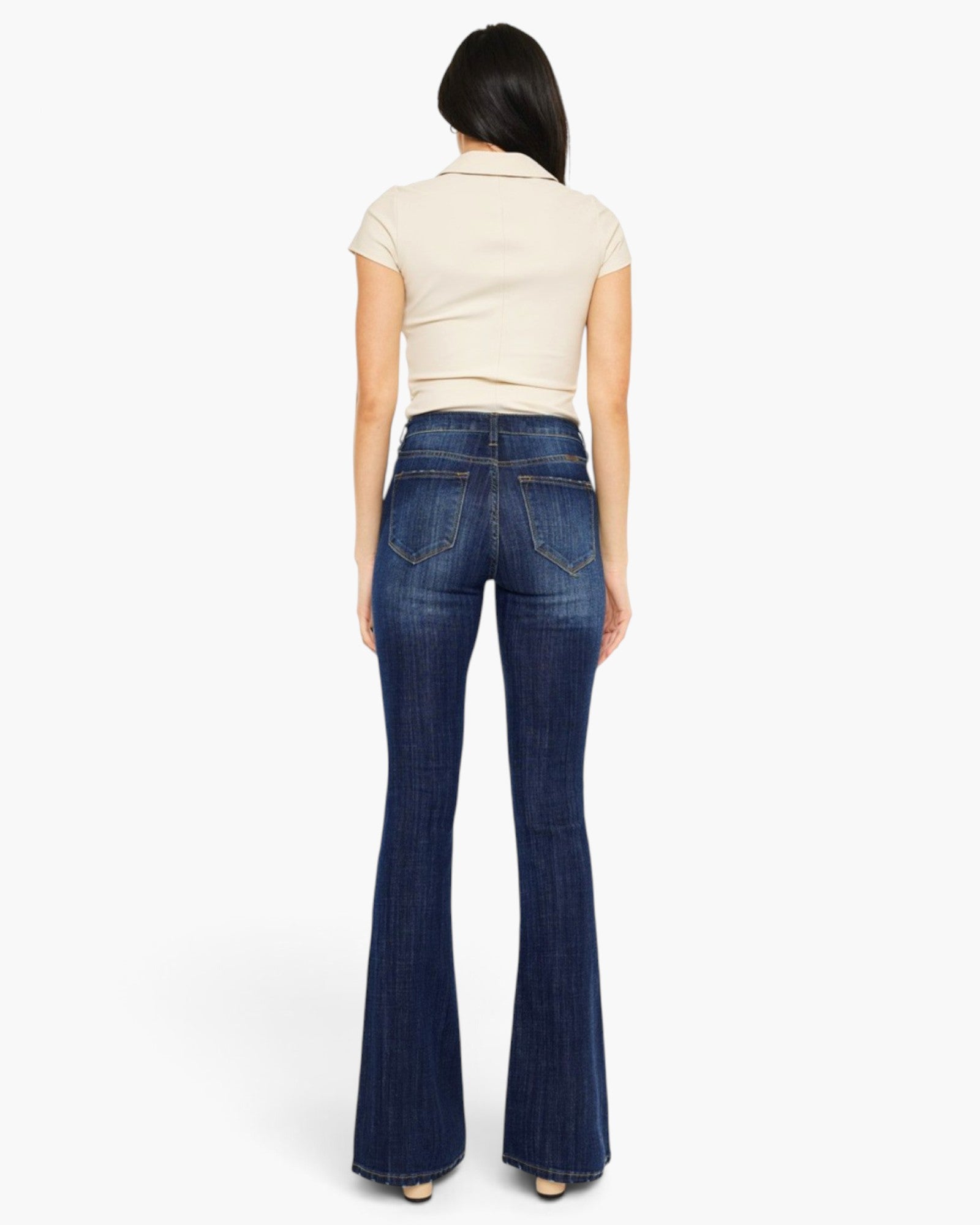 A woman shown from the back wearing dark blue flared jeans and a cream short-sleeve top, standing against a plain light gray studio background.