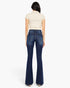 A woman shown from the back wearing dark blue flared jeans and a cream short-sleeve top, standing against a plain light gray studio background.