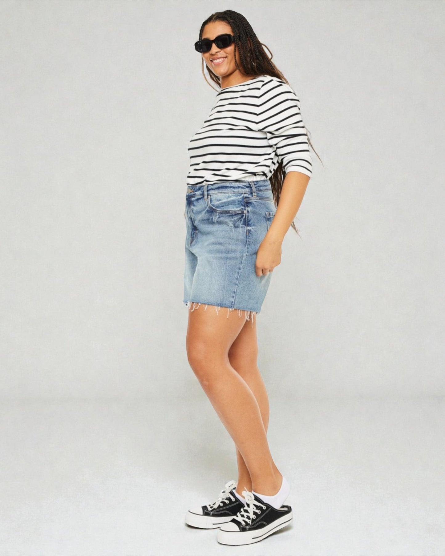 Woman wearing a striped shirt, denim skirt, and black sneakers on a plain background