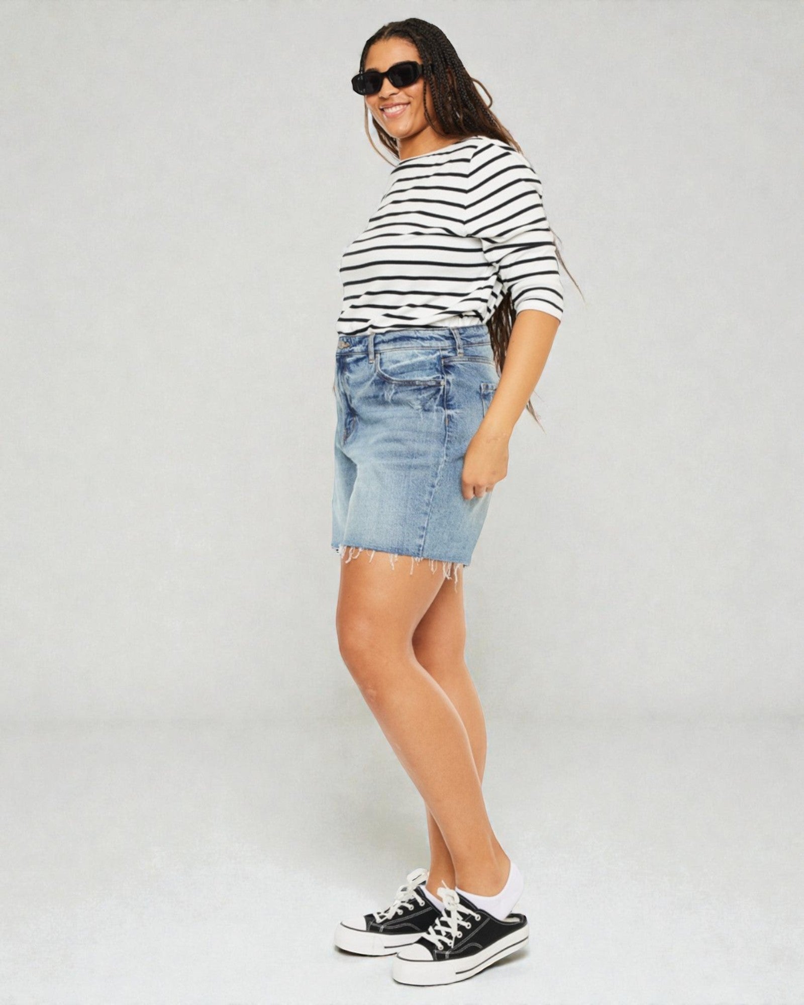 Woman wearing a striped shirt, denim skirt, and black sneakers on a plain background