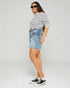 Woman wearing a striped shirt, denim skirt, and black sneakers on a plain background