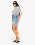A woman modeling a black and white striped short-sleeve t-shirt, a light-wash denim mini skirt, and black low-top sneakers against a plain white background.