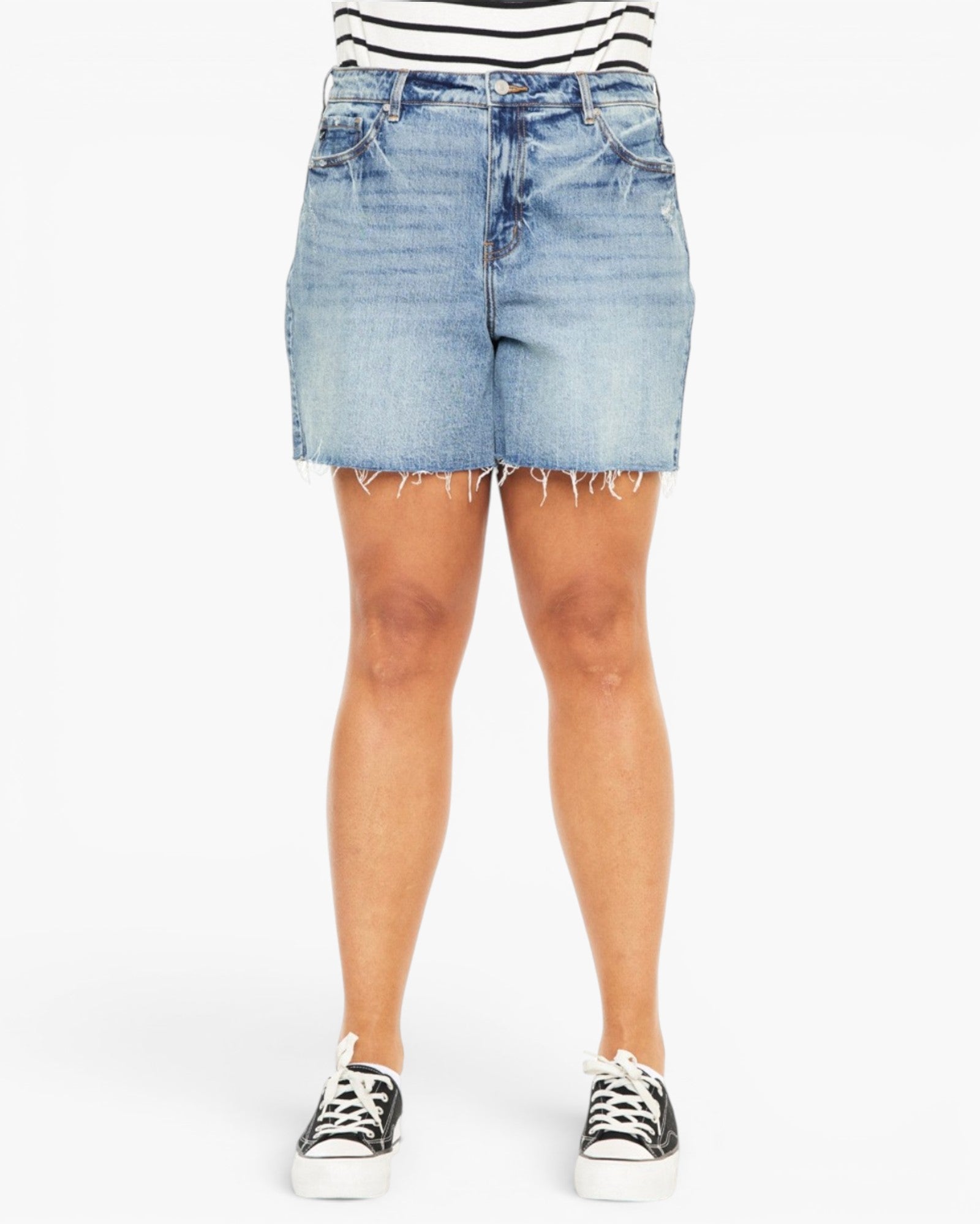 A person wearing light-wash blue denim shorts with a frayed hem, paired with a black-and-white striped top and black low-top sneakers, shown against a plain light gray studio background.