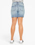 Rear view of a person wearing a light blue denim mini skirt with a frayed hem, paired with a black and white striped top and black slip-on shoes, against a plain white studio background.