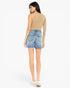 A woman shown from the back wearing a beige long-sleeve crop top and light-wash denim shorts, paired with white platform sneakers, against a plain white studio background.