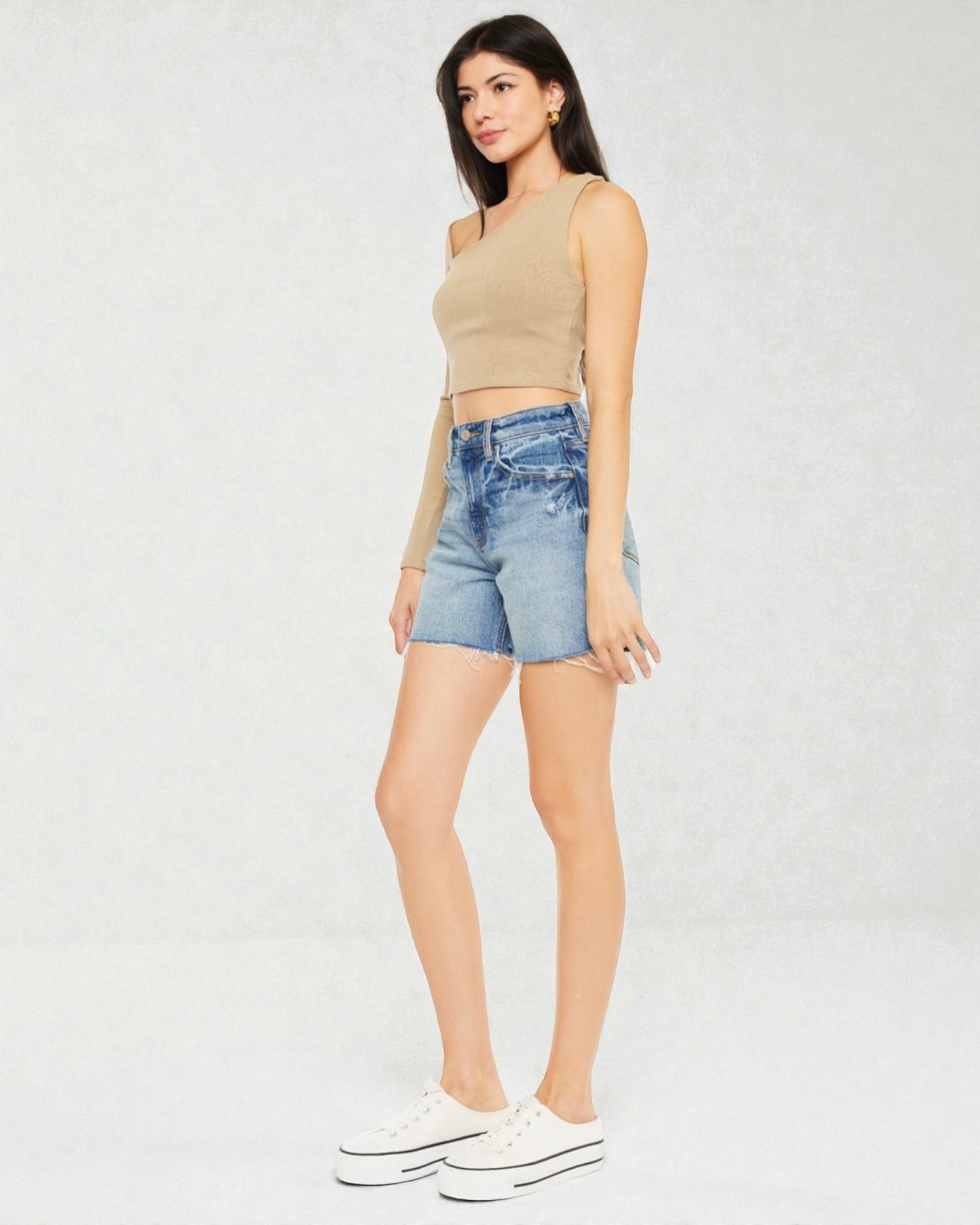 Woman wearing a beige sleeveless top and denim shorts on a white background