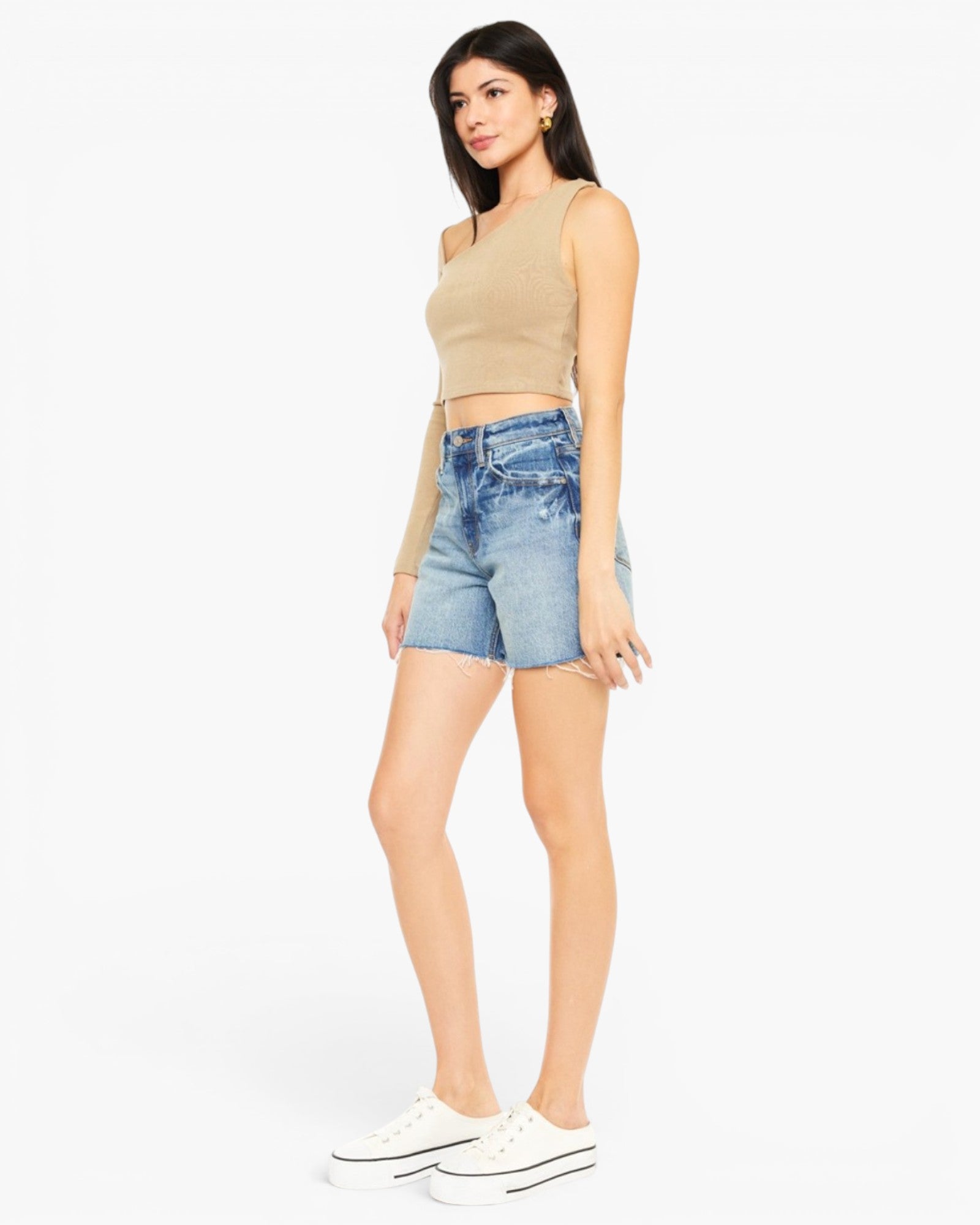A woman modeling a beige ribbed knit crop top and light-wash blue denim shorts against a plain white studio background.