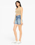 A woman modeling a beige ribbed knit crop top and light-wash blue denim shorts against a plain white studio background.