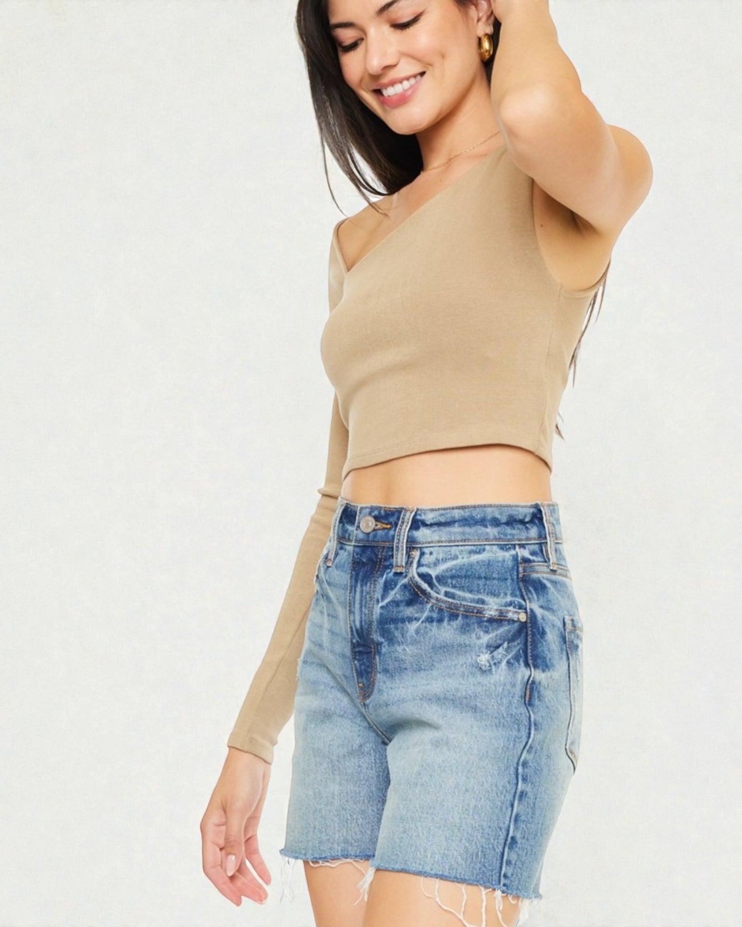 Woman wearing a beige crop top and denim shorts on a white background