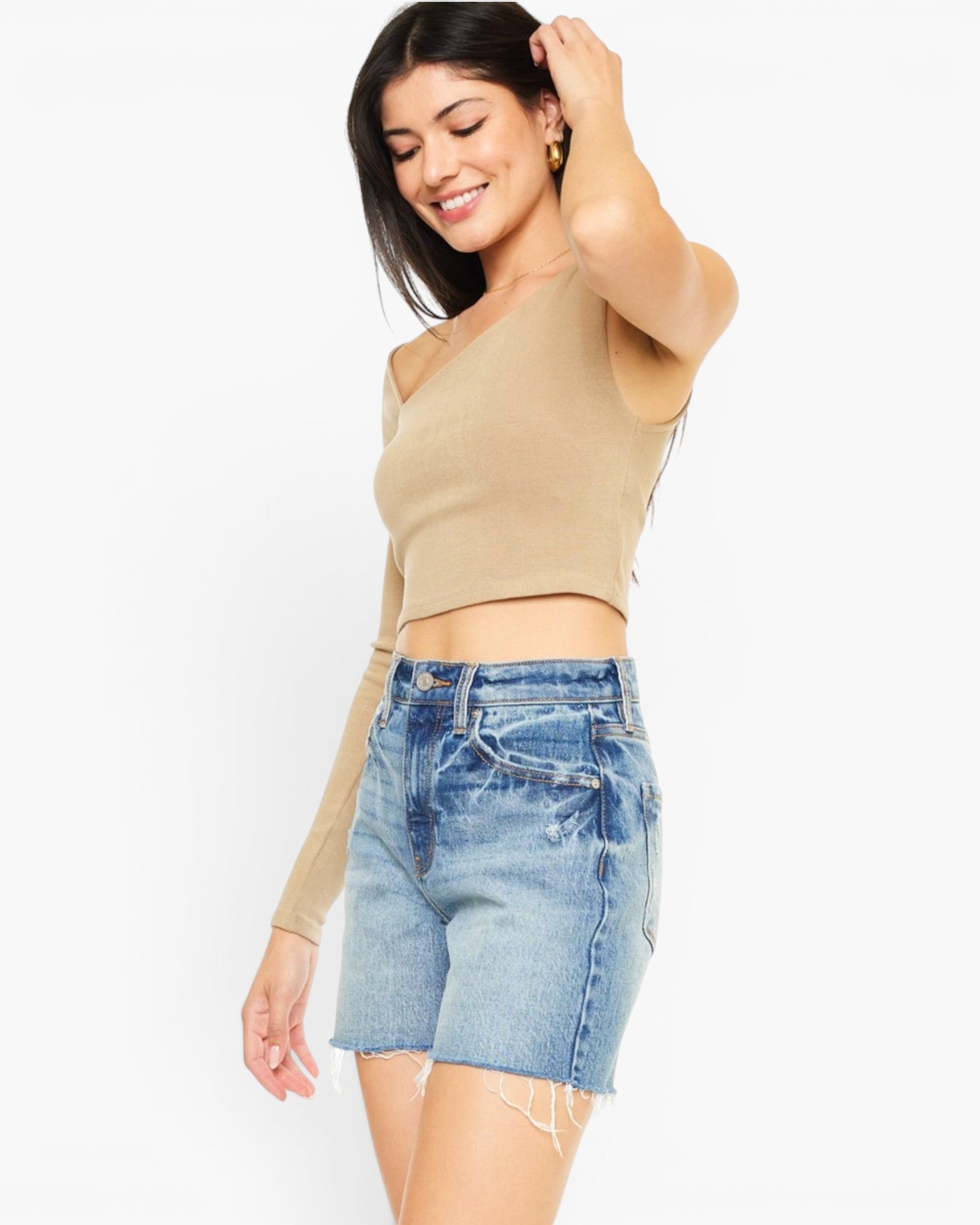 A woman modeling a beige long-sleeve crop top and light blue denim shorts against a plain white background.