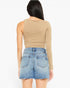 A woman shown from the back wearing a beige long-sleeve crop top and light blue denim shorts against a plain white background.