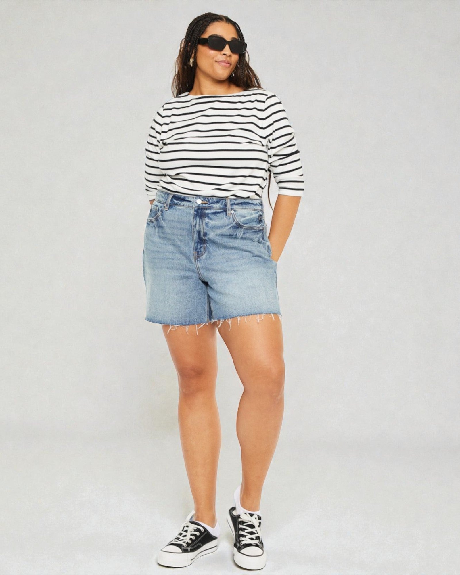 Woman wearing a striped shirt and denim shorts on a plain background