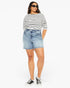 A woman modeling a black and white horizontally striped short-sleeve t-shirt, light-wash blue denim shorts with raw hems, black sunglasses, and black low-top sneakers against a plain white studio background.