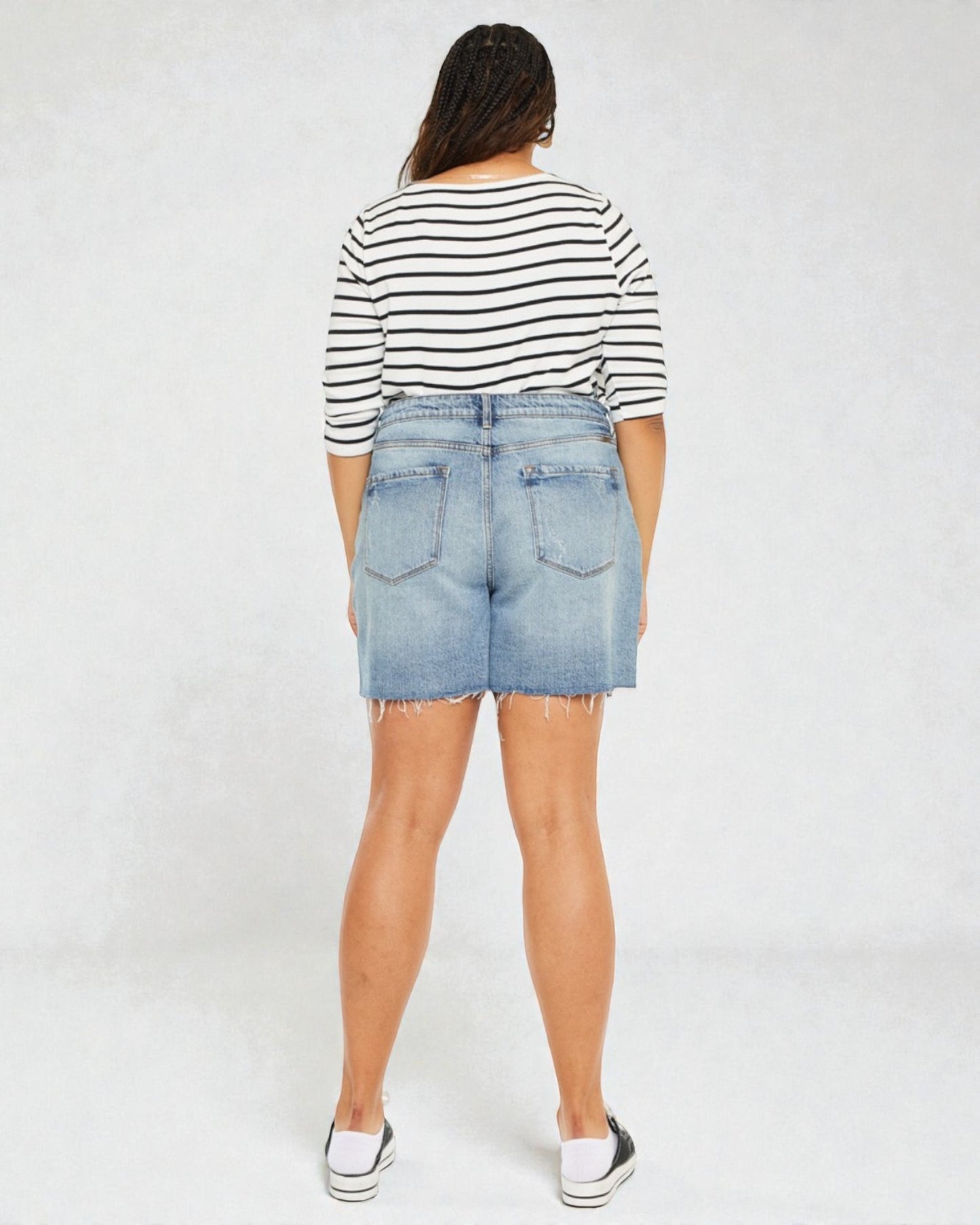 Person wearing a striped shirt and denim shorts on a white background