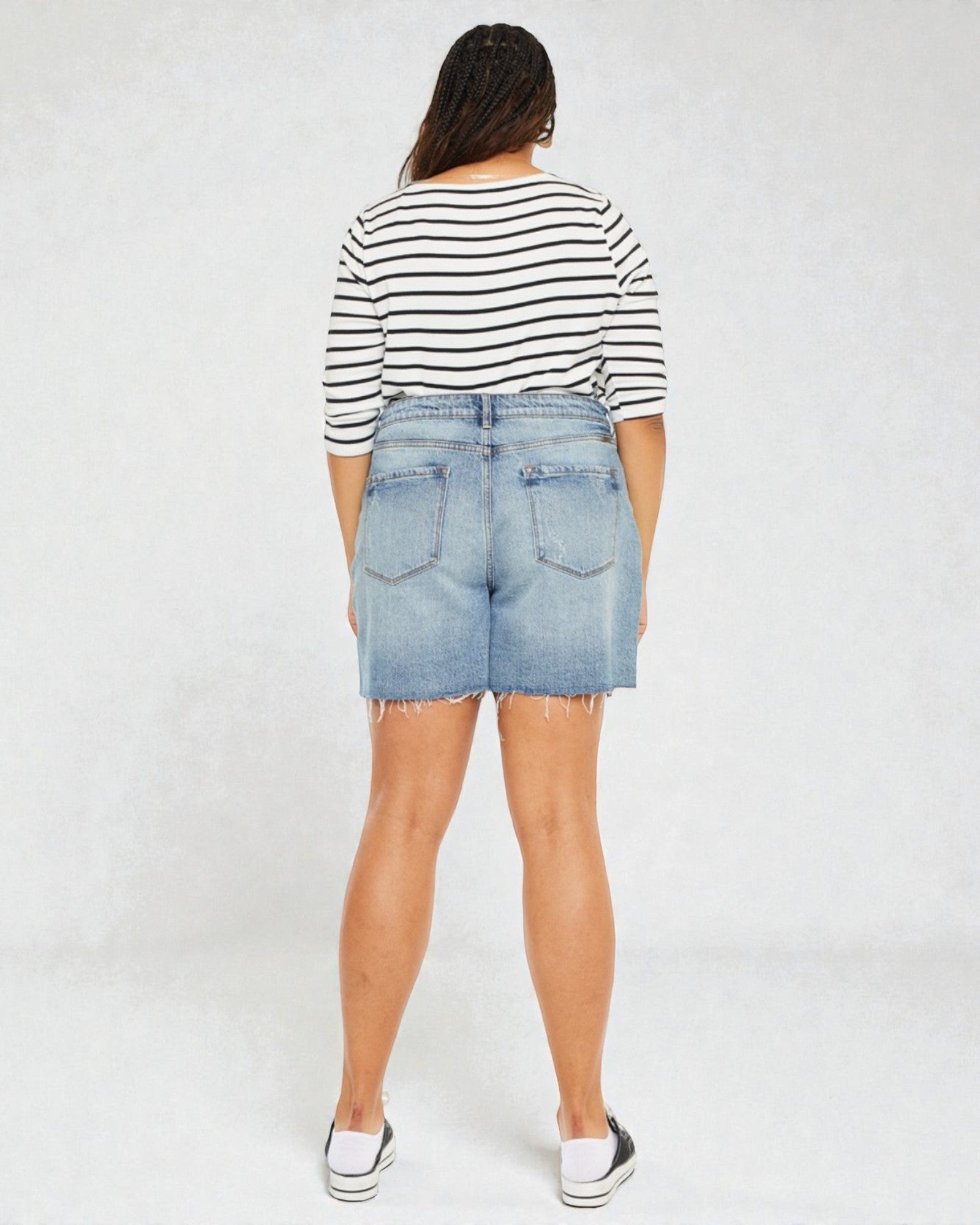 Person wearing a striped shirt and denim shorts on a white background