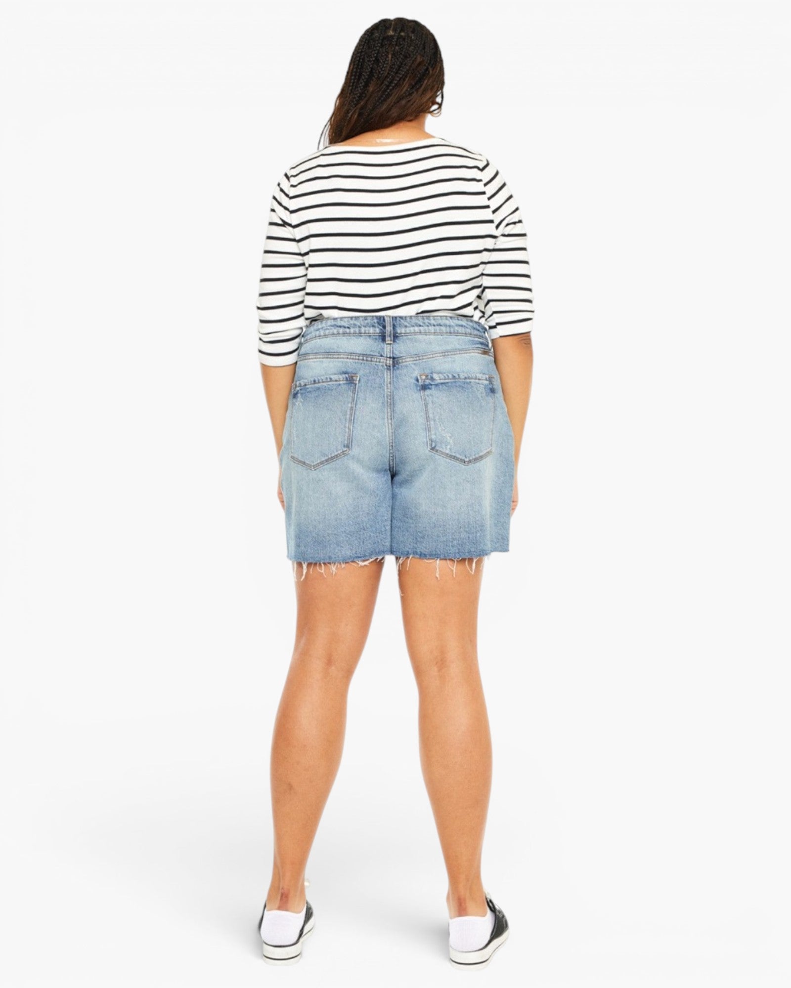 A model shown from the back wearing a black and white striped short-sleeve top, light blue denim shorts, and white slip-on shoes against a plain white background.