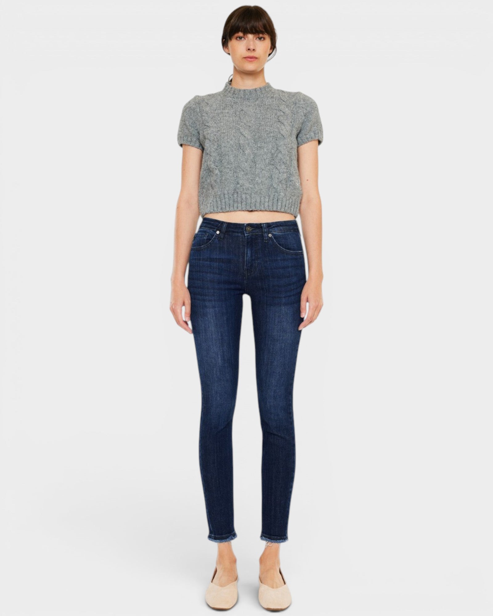 Woman wearing dark blue jeans and a gray cropped top on a white background