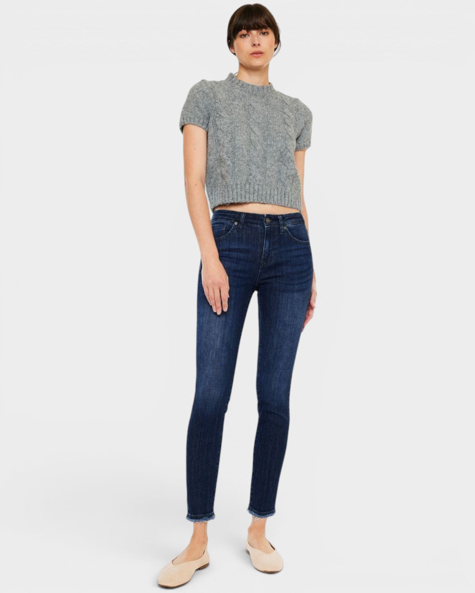 Woman wearing a gray sweater and dark blue jeans on a white background
