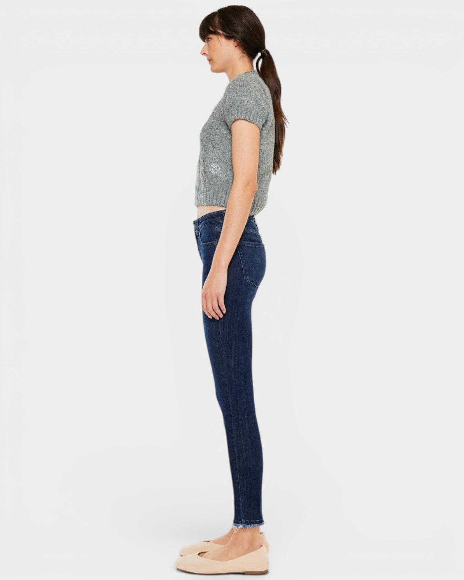 Woman wearing a gray sleeveless top and dark blue jeans on a white background