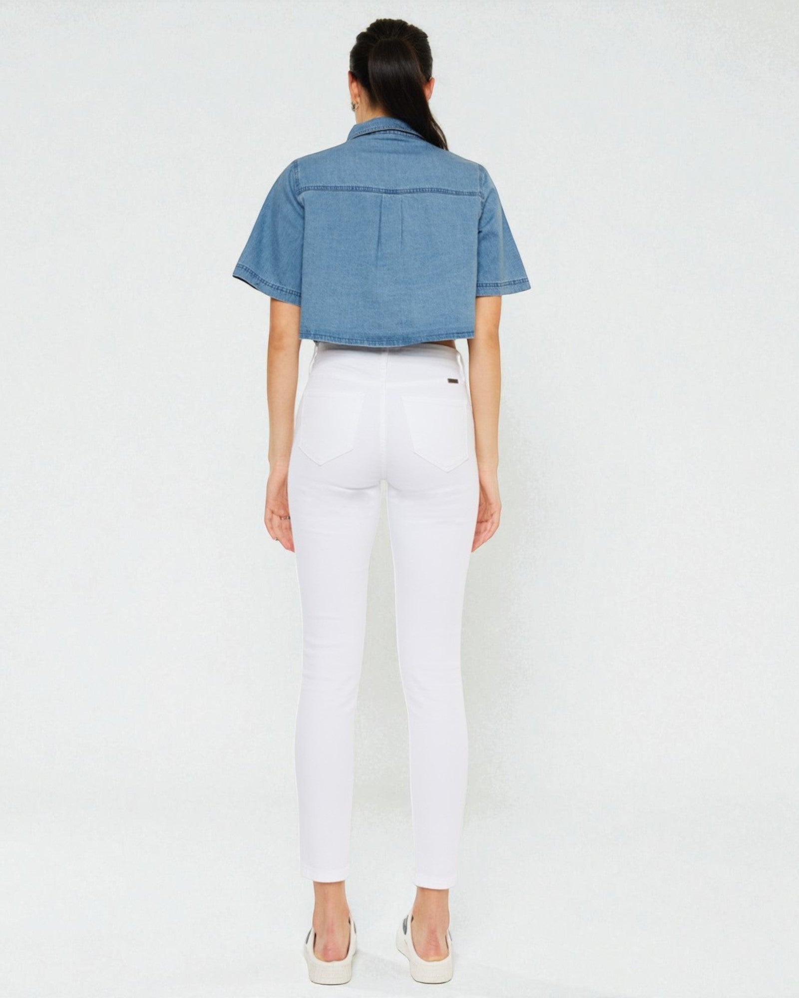 Person wearing a denim shirt and white pants on a plain background