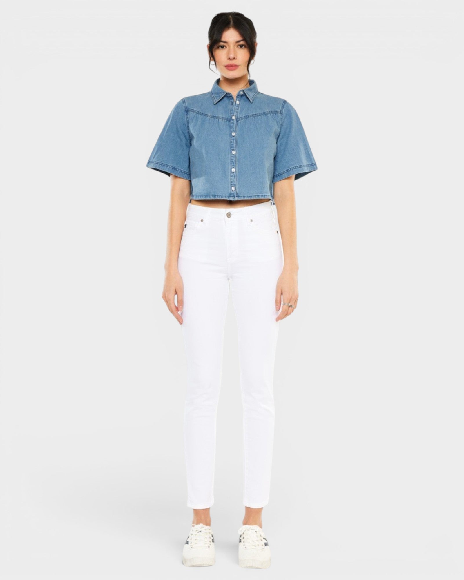 Woman wearing a blue denim shirt and white pants on a light gray background