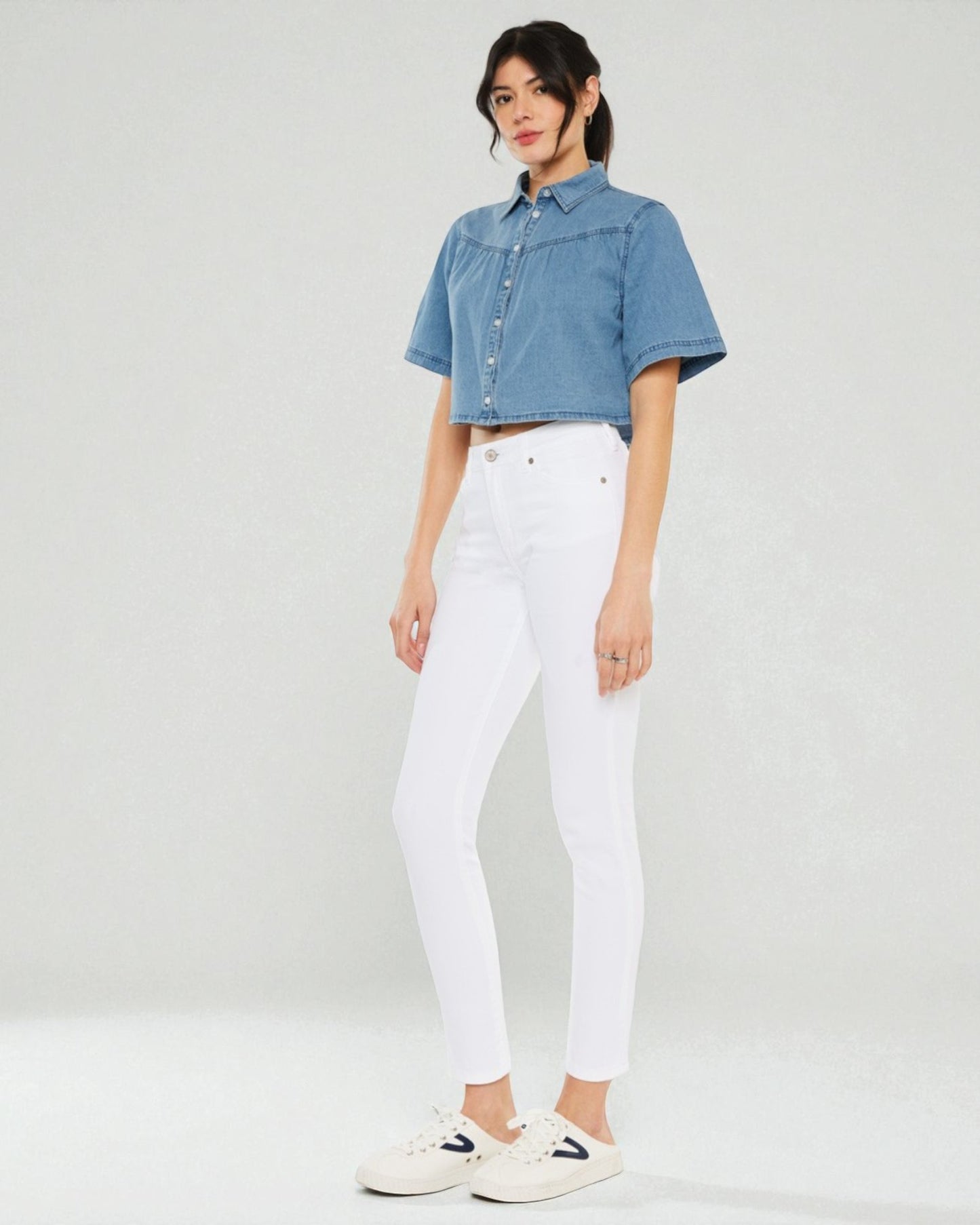 Woman wearing a denim shirt and white pants on a plain background