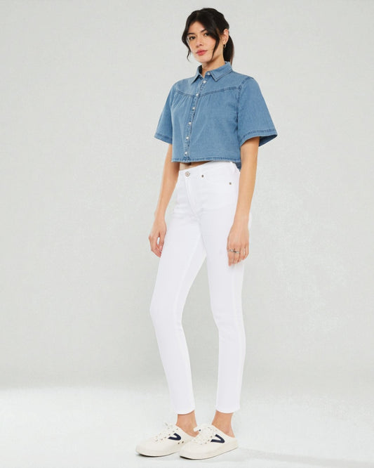 Woman wearing a denim shirt and white pants on a plain background