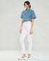 Woman wearing a denim shirt and white pants on a plain background