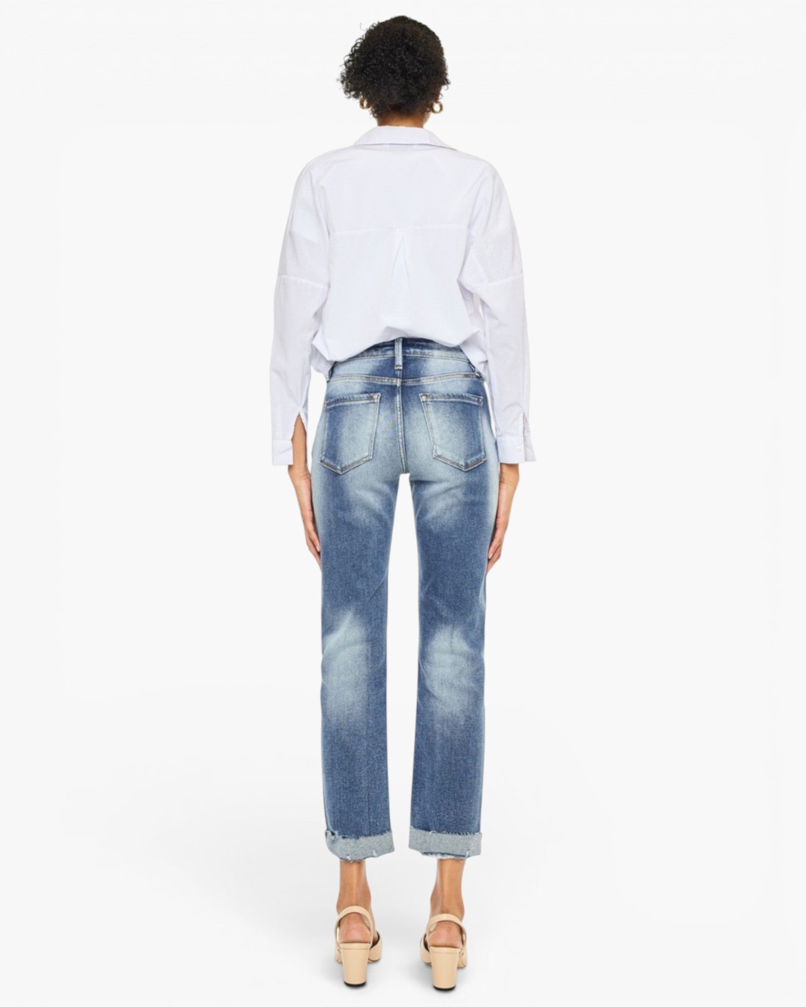 A model shown from the back wearing light-wash blue cropped jeans with a faded wash, a white button-up shirt, and beige wedge sandals against a plain white background.