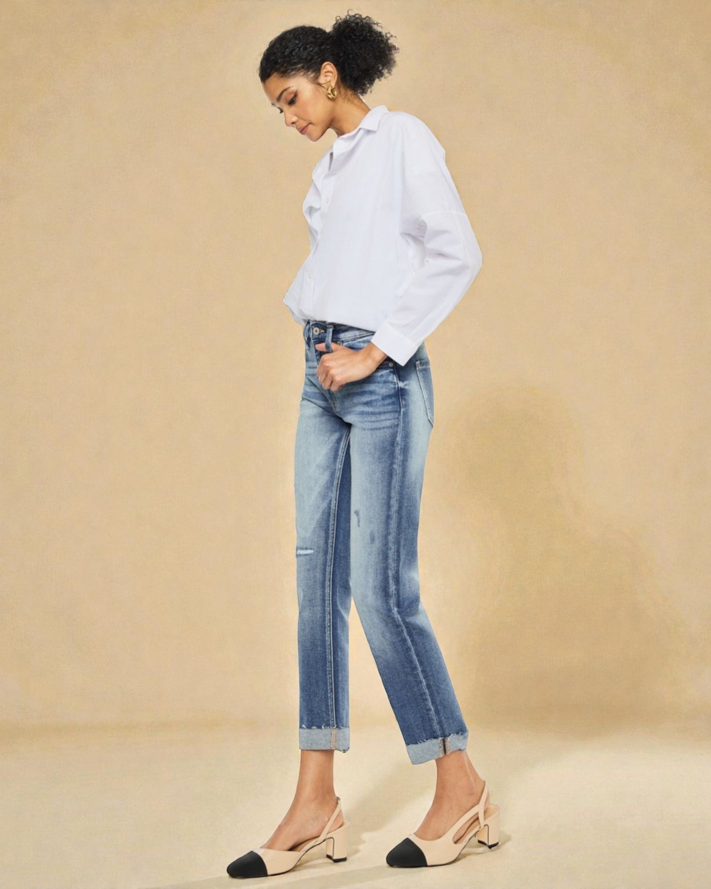 Woman wearing a white shirt and light blue jeans against a beige background